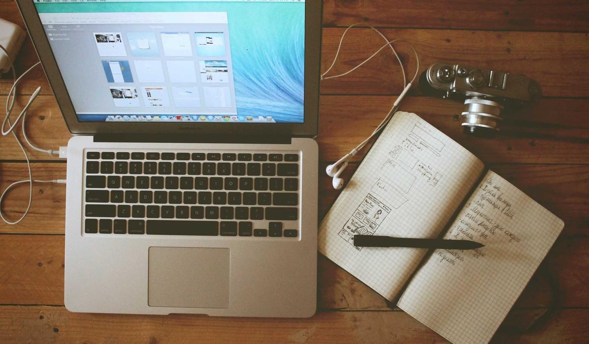 A writing desk with a laptop, camera, and notebook full of sketches
